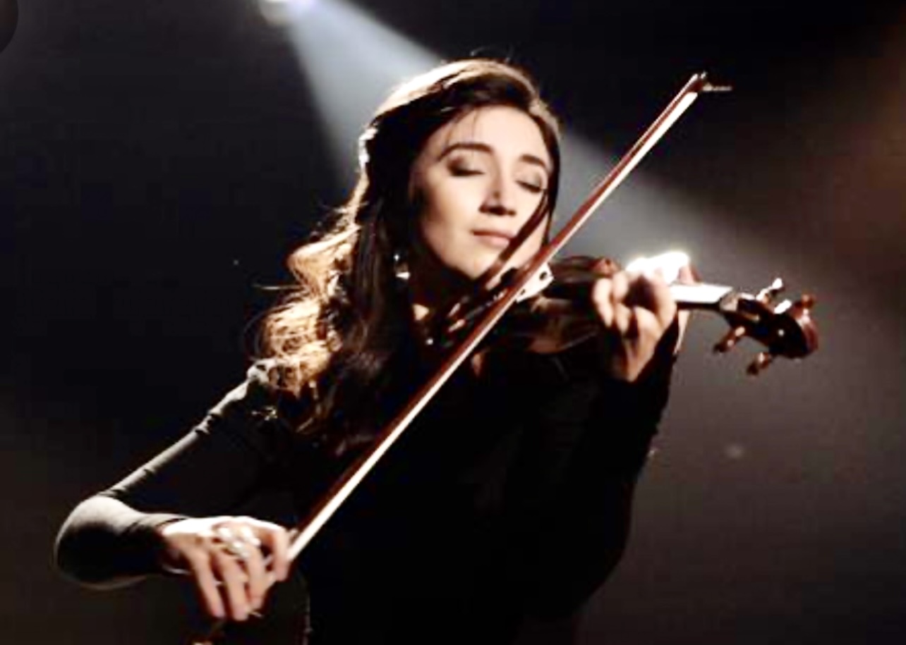 Une femme interprétant de la musique classique devant un projecteur, jouant gracieusement du violon.