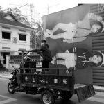 Une photo en noir et blanc d'un homme faisant du vélo avec une photo de deux enfants dessus, prise au Cambodge.