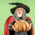 Un homme habillé en sorcière tenant une citrouille pour Halloween.