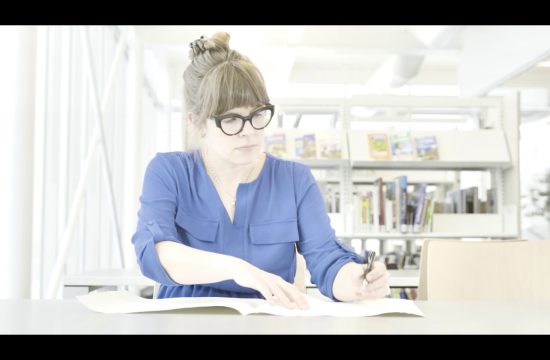 Une femme à lunettes écrivant un livre sur la Littérature québécoise dans une bibliothèque.