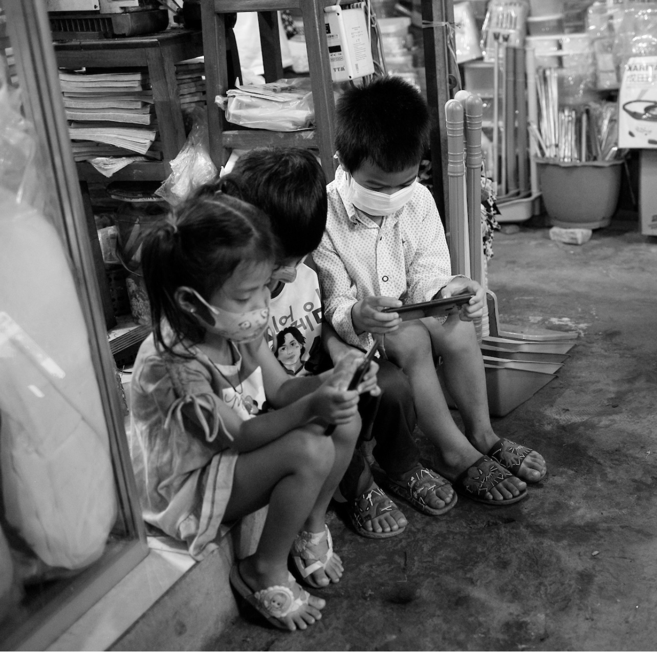 Trois enfants assistent devant un magasin avec des masques, photos du Cambodge.
