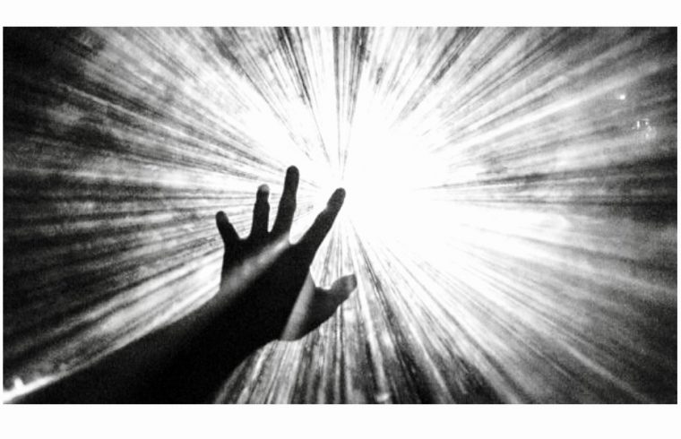 Une photo en noir et blanc d’une main tendant la main vers une lumière, évoquant un sentiment de philosophie.