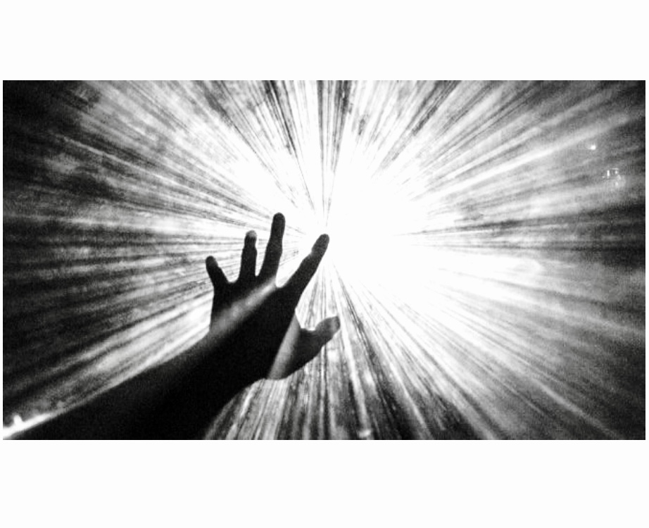 Une photo en noir et blanc d’une main tendant la main vers une lumière, évoquant un sentiment de philosophie.