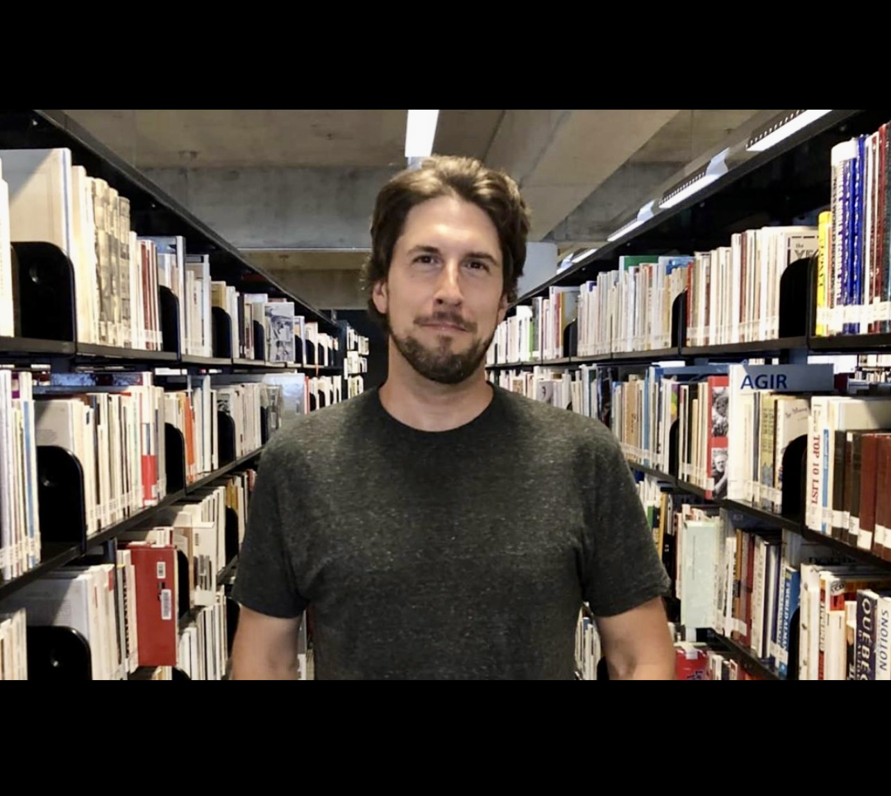 Un homme debout devant une étagère remplie de Littérature québécoise dans une bibliothèque.