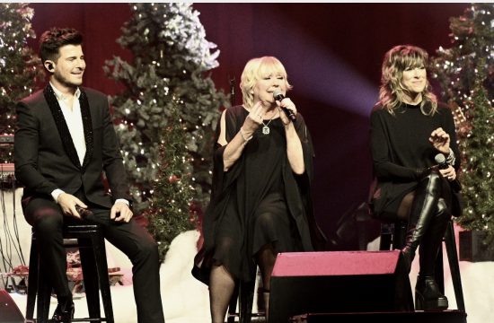 Trois personnes chantant Noël devant un sapin de Noël.
