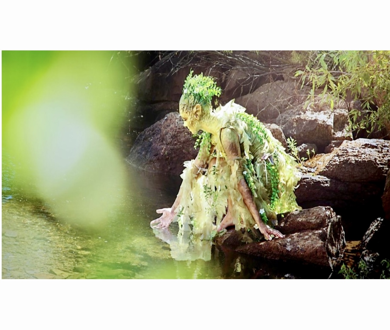 Une femme vêtue d’une robe verte est assise avec philosophie sur un rocher dans l’eau.