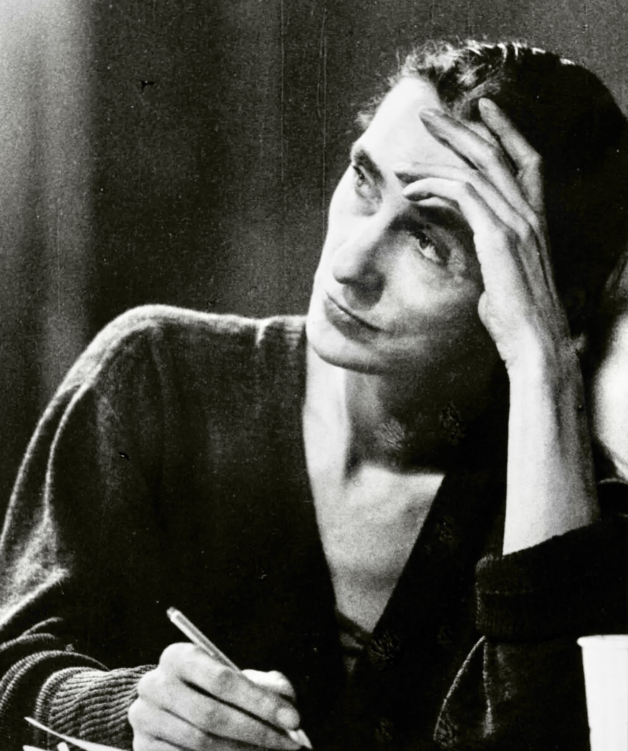 Une photo en noir et blanc d'une femme écrivant à un bureau, capturant l'essence de son mouvement gracieux et de son expression artistique contemporaine.