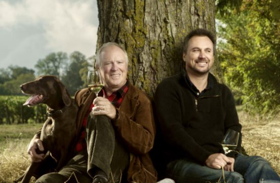 Deux hommes assis sous un arbre avec un chien, dégustant un verre de Chablis bien frais de Jean-Marc Brocard.