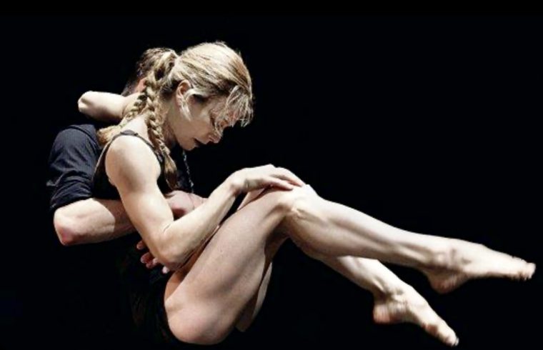 Un homme et une femme se déplacent avec grâce sur un fond noir, leurs corps s'entrelaçant dans des mouvements fluides, incarnant l'essence de la danse contemporaine.