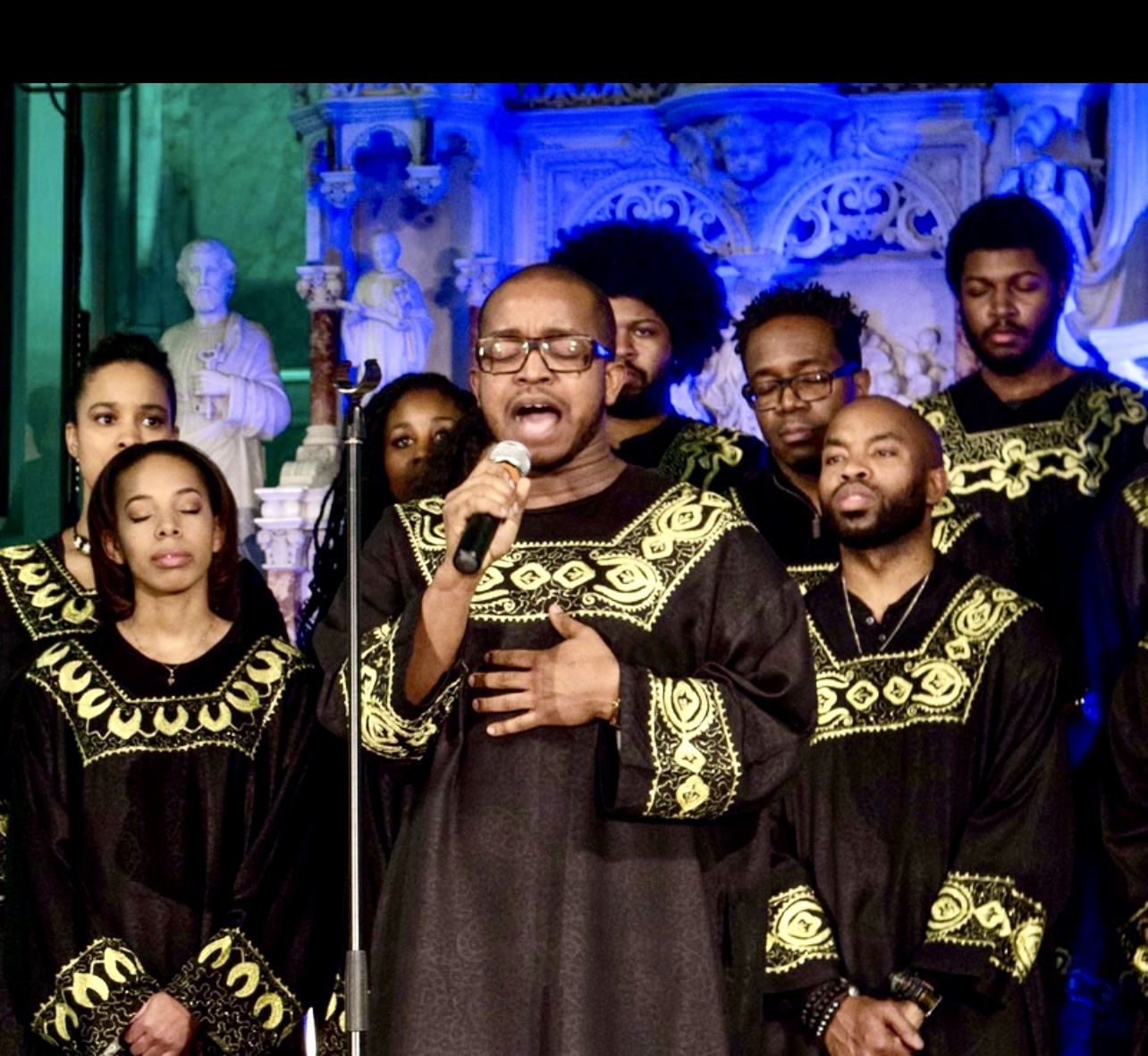 Un groupe d'hommes en robes noires chantant dans un microphone, mettant en valeur les traditions culturelles pendant la Quoi Faire Semaine.