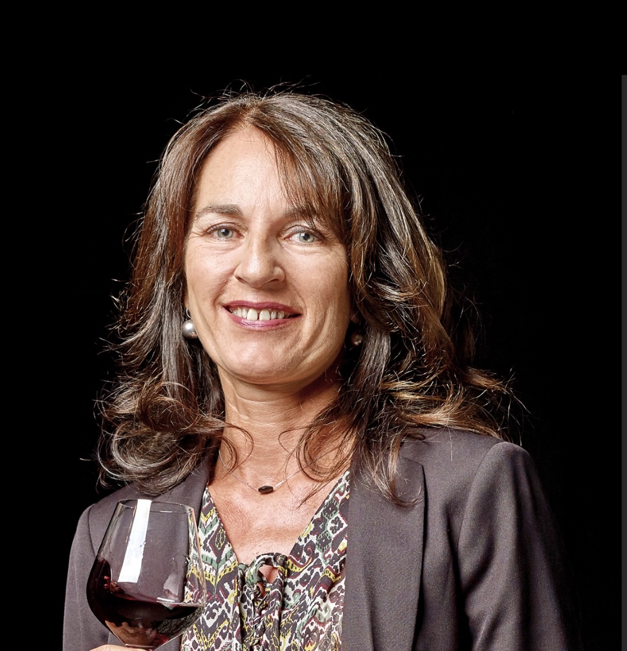 Une femme de La Fiole tenant un verre de vin devant un fond noir.