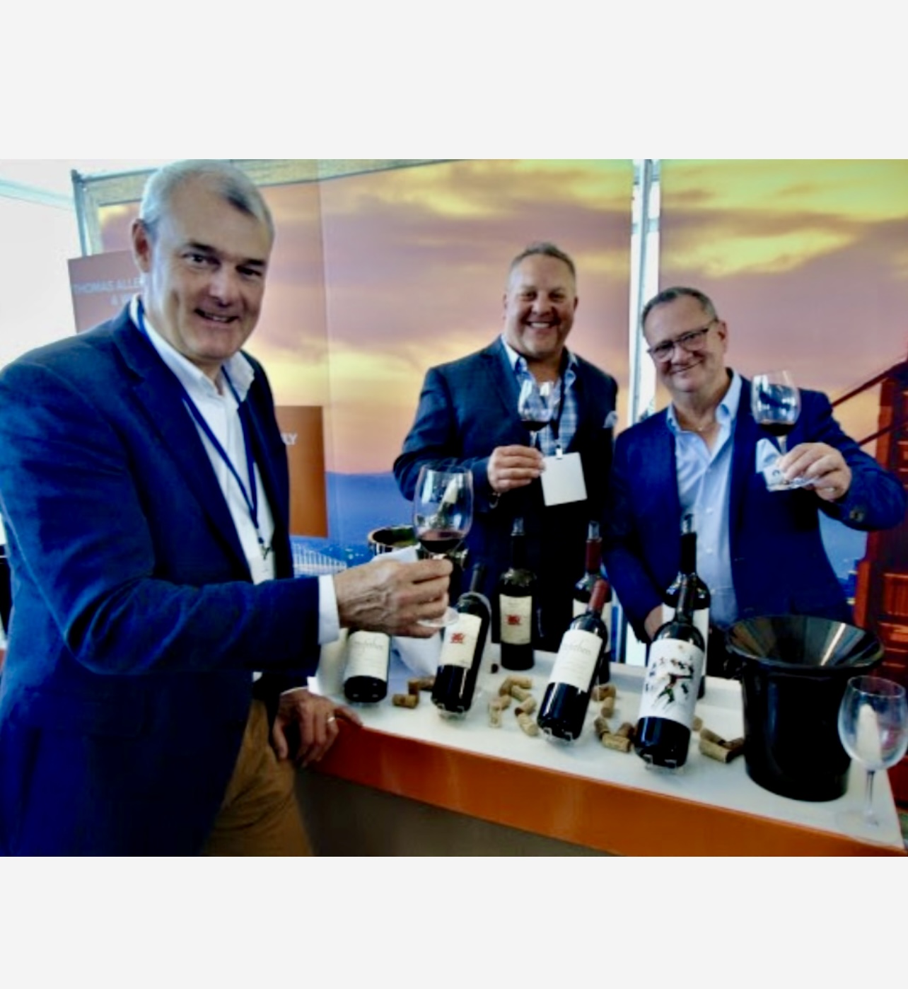 Trois hommes debout devant une table avec des bouteilles de vin de la collection Vins de Californie 2023.