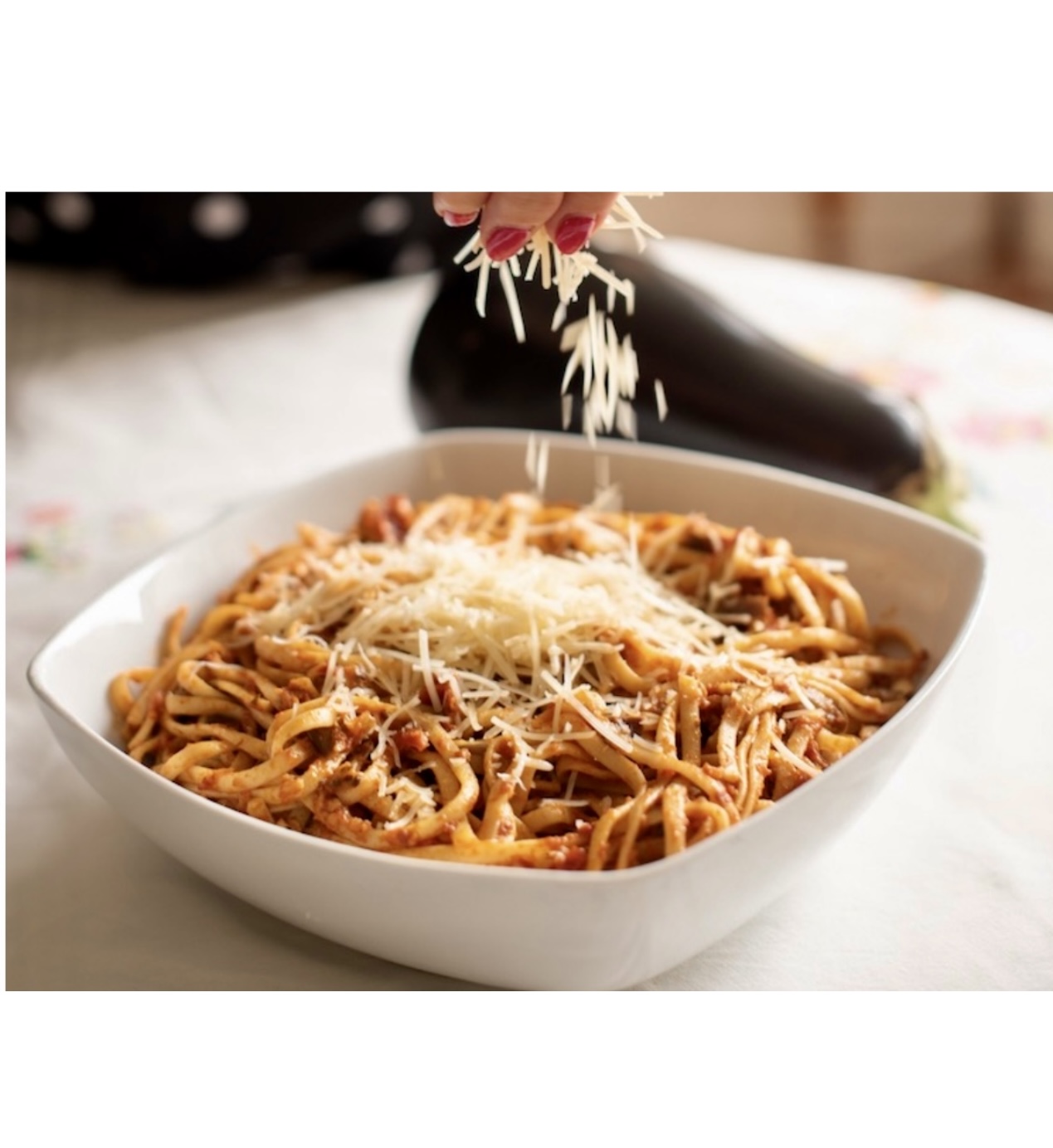 Une personne arrosant du parmesan sur un bol de Linguini à la sauce tomate et spaghetti aubergine.