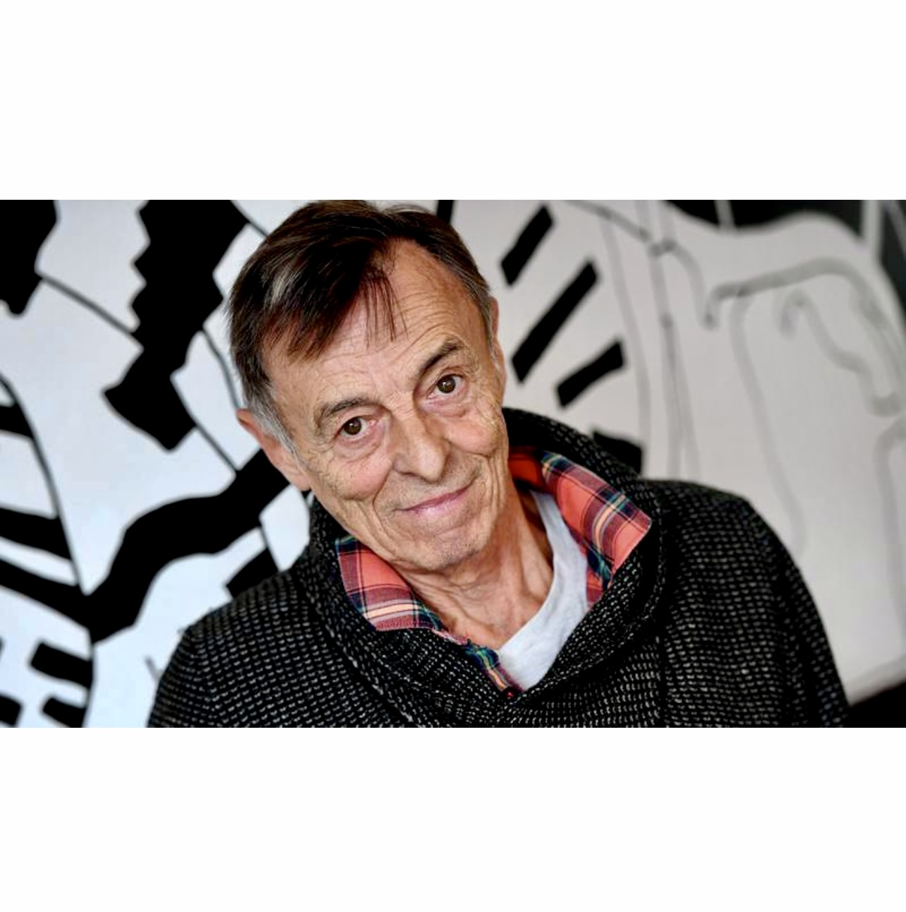 Robert Lalonde, un homme plus âgé, souriant devant un tableau en noir et blanc.
