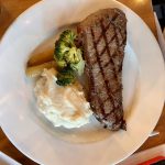 Un steak du Vieux-Port Steakhouse avec du brocoli et de la purée de pommes de terre dans une assiette.