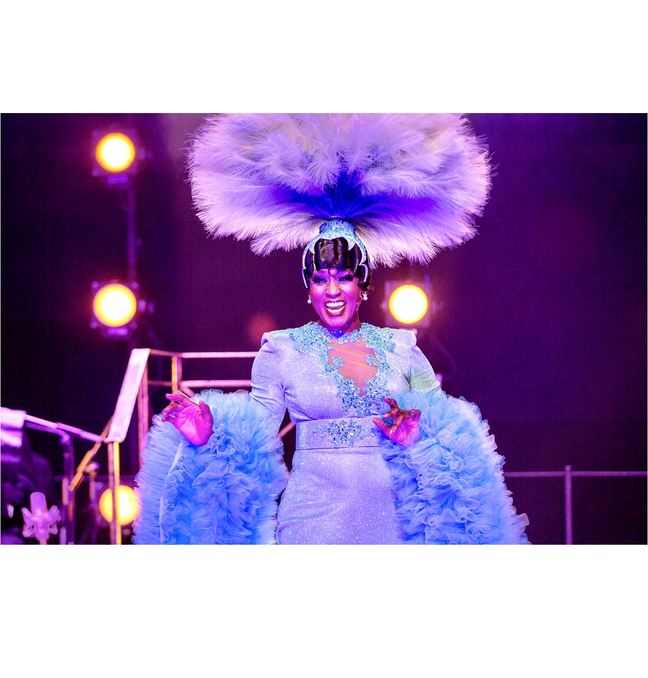 Joséphine, une femme en robe bleue avec des plumes sur la tête, joue dans la comédie musicale à voir !