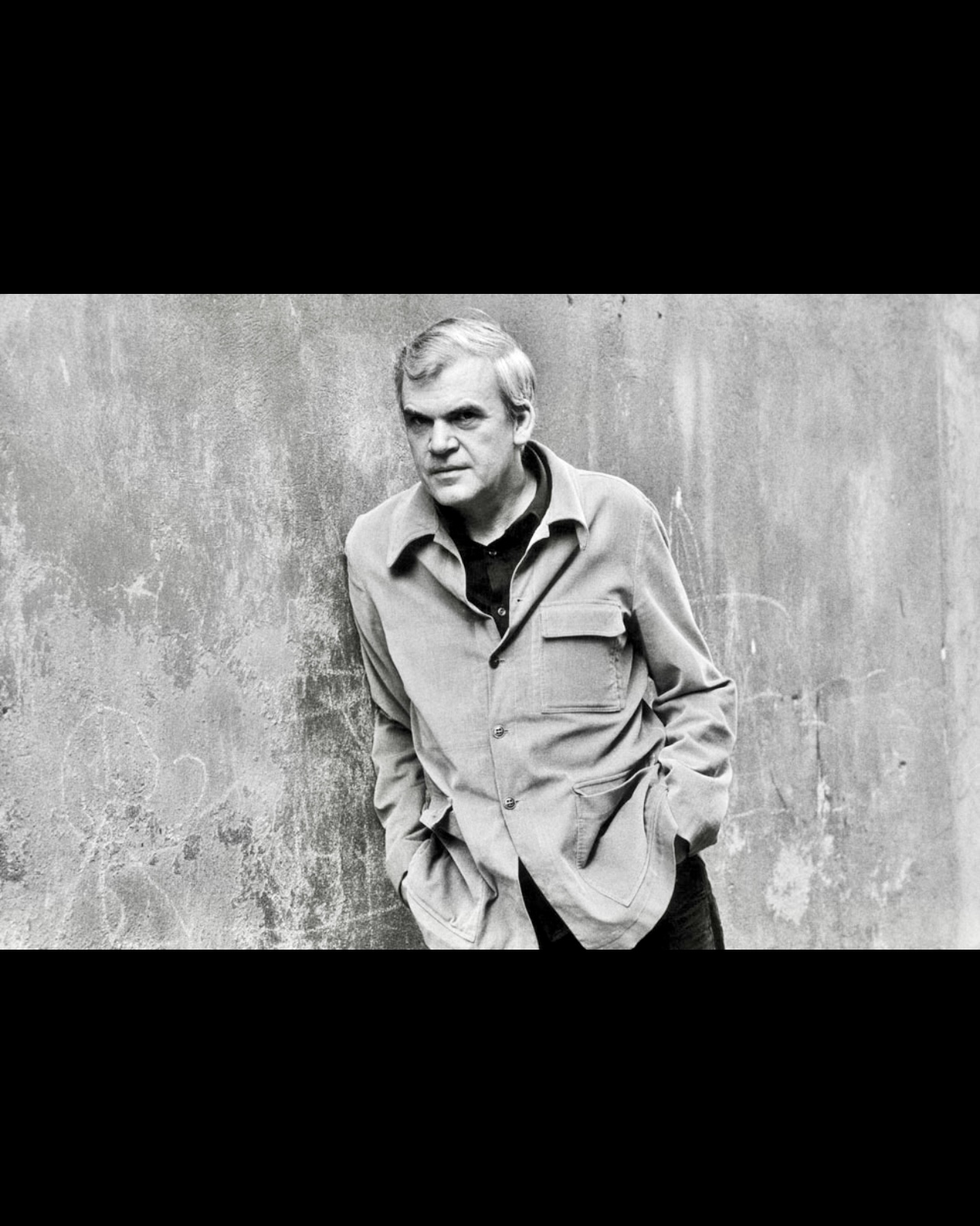 Photo en noir et blanc d'un homme adossé à un mur, rendant hommage à Milan Kundera.