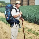 Un homme avec un sac à dos et des bâtons sur le chemin des découvertes de Compostelle.