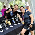 Un homme et une femme posant gracieusement pour une photo devant une table remplie de bouteilles de vin au Festival Vins.