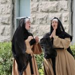 Deux religieuses vêtues de noir et de marron participent à une représentation du Théâtre déambulatoire à Gatineau, debout devant un édifice.