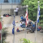 Un groupe de sans-abri assis par terre près des drapeaux.