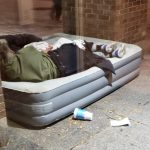 Un sans-abri dormant sur un matelas gonflable devant un magasin.