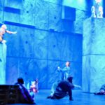 Un groupe d'acrobates sur scène devant un mur bleu, exécutant une interprétation énergique de Notre Dame de Paris.