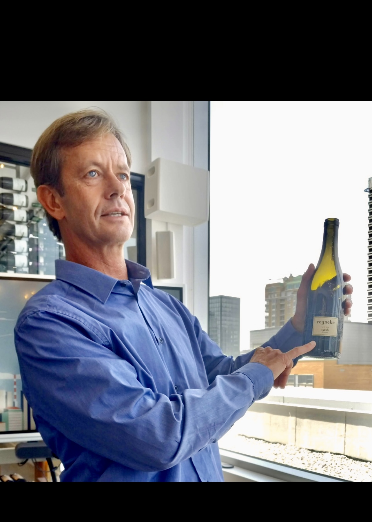 Un homme tenant une bouteille de vin Reyneke devant une fenêtre.