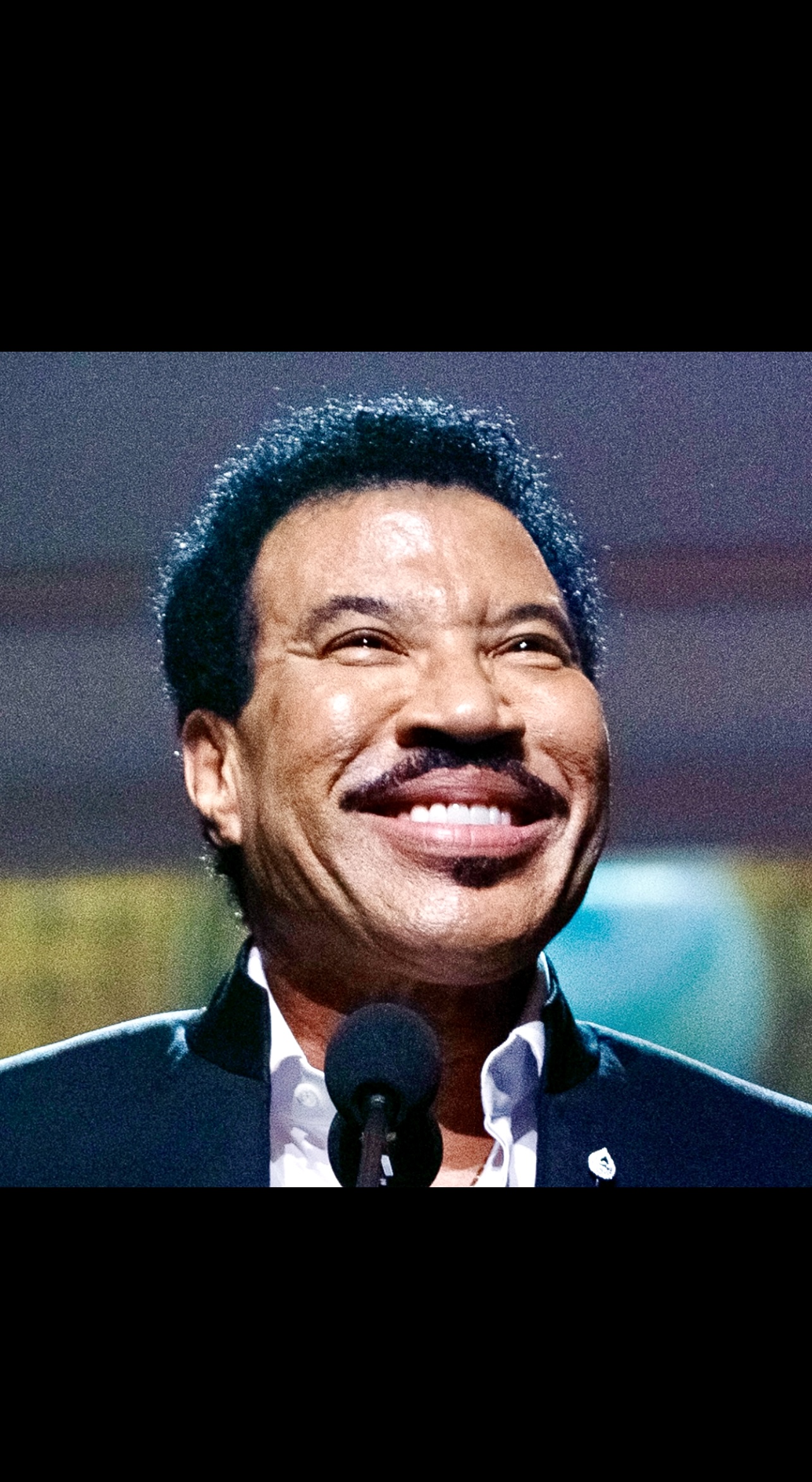 Lionel Richie sourit dans un micro lors d'une performance électrisante.
