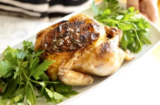 Une personne tient un poulet dans une assiette et sert des Poulets de Cornouailles au miel et à l'érable.