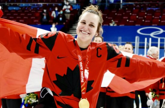 Une femme tenant un drapeau canadien et une médaille d'or dans le hockey professionnel au féminin.