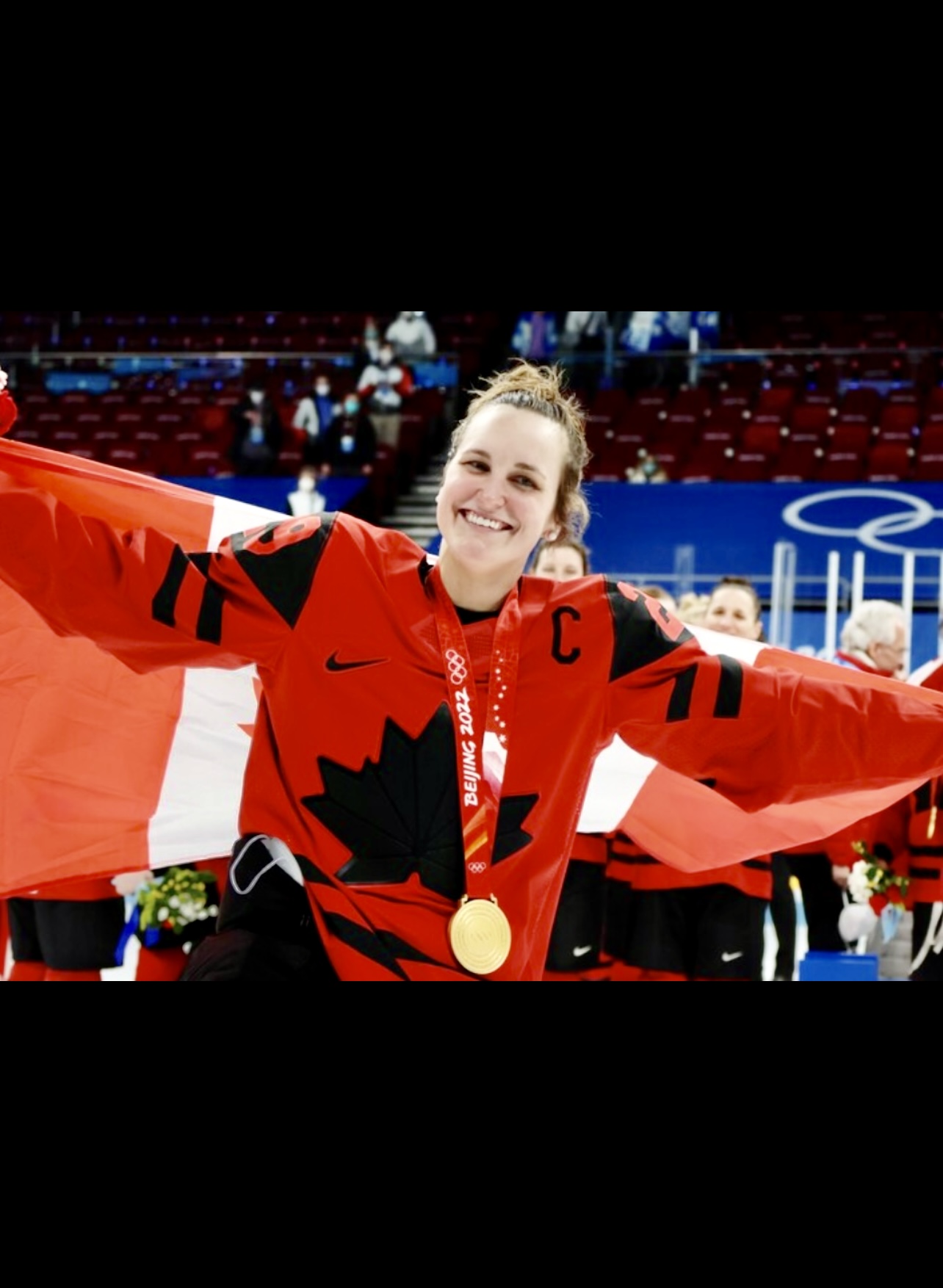 Une femme tenant un drapeau canadien et une médaille d'or dans le hockey professionnel au féminin.