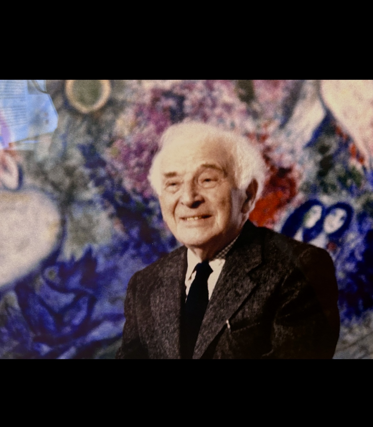 Un homme en costume-cravate sourit devant un tableau de Chagall.