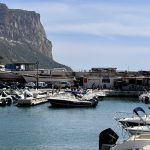 Dans le port pittoresque de Cassis, des bateaux amarrés paisiblement dans les eaux azurées, encadrés par la présence majestueuse d'une montagne en arrière-plan, invitant les visiteurs à ressentir la douceur de
