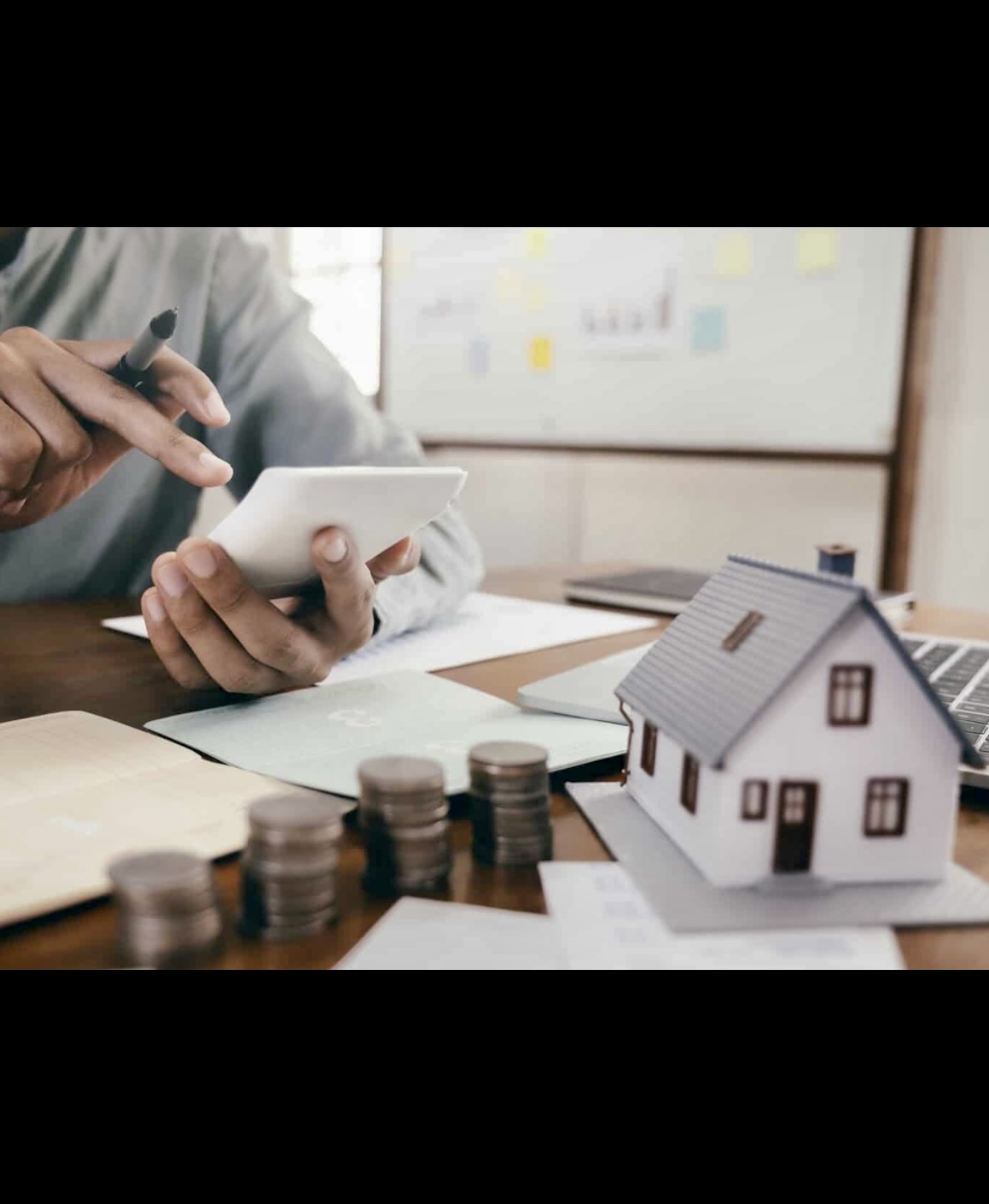 Un homme utilisant son téléphone assis à une table avec de l’argent et un modèle de maison, explorant les options de consolidation de dettes par l’hypothèque.