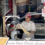 Une femme en tablier blanc prépare des pâtes devant une fenêtre tout en surplombant le charmant paysage urbain de Lucques.