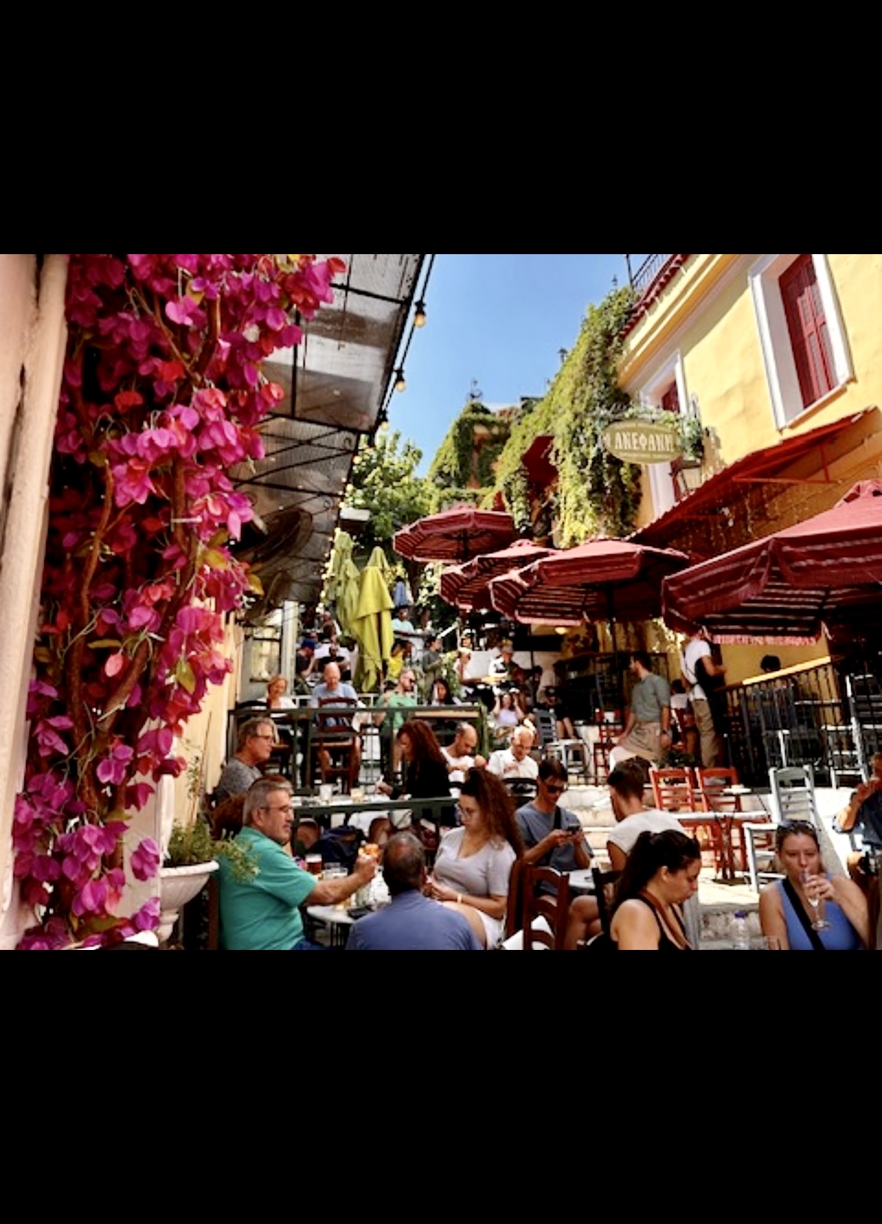Un groupe de personnes assises à des tables dans un café en plein air en Grèce, une expérience inoubliable et fort intéressante.