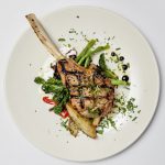 Les côtelettes d'agneau grillées sur une assiette blanche de Quattro mettent en valeur leur gastronomie exceptionnelle et leur ambiance accueillante.