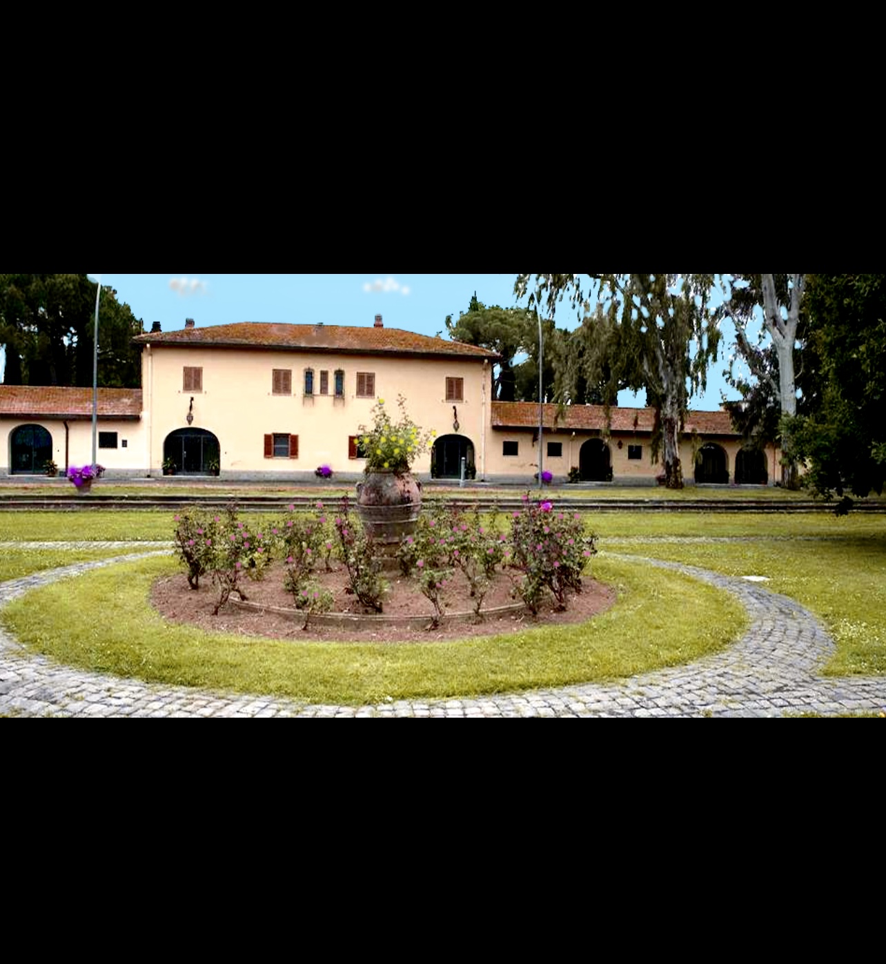Un grand bâtiment avec un jardin fleuri en face, proposant une sélection de vins Vins de Casale del Giglio.