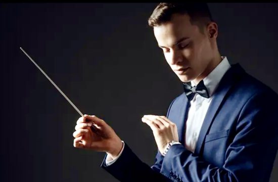 Un homme en smoking tenant une baguette de chef d'orchestre tout en dirigeant la Symphonie n° 9 de Beethoven.