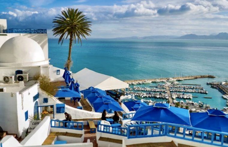Un bâtiment blanc avec des parasols bleus surplombant l'océan à La Tunisie au Salon tourisme et voyage.