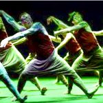 Un groupe fascinant de danseurs se produisant sur une scène verte vibrante, mettant en valeur la chorégraphie captivante du « Livre de la jungle d’Akram Khan.