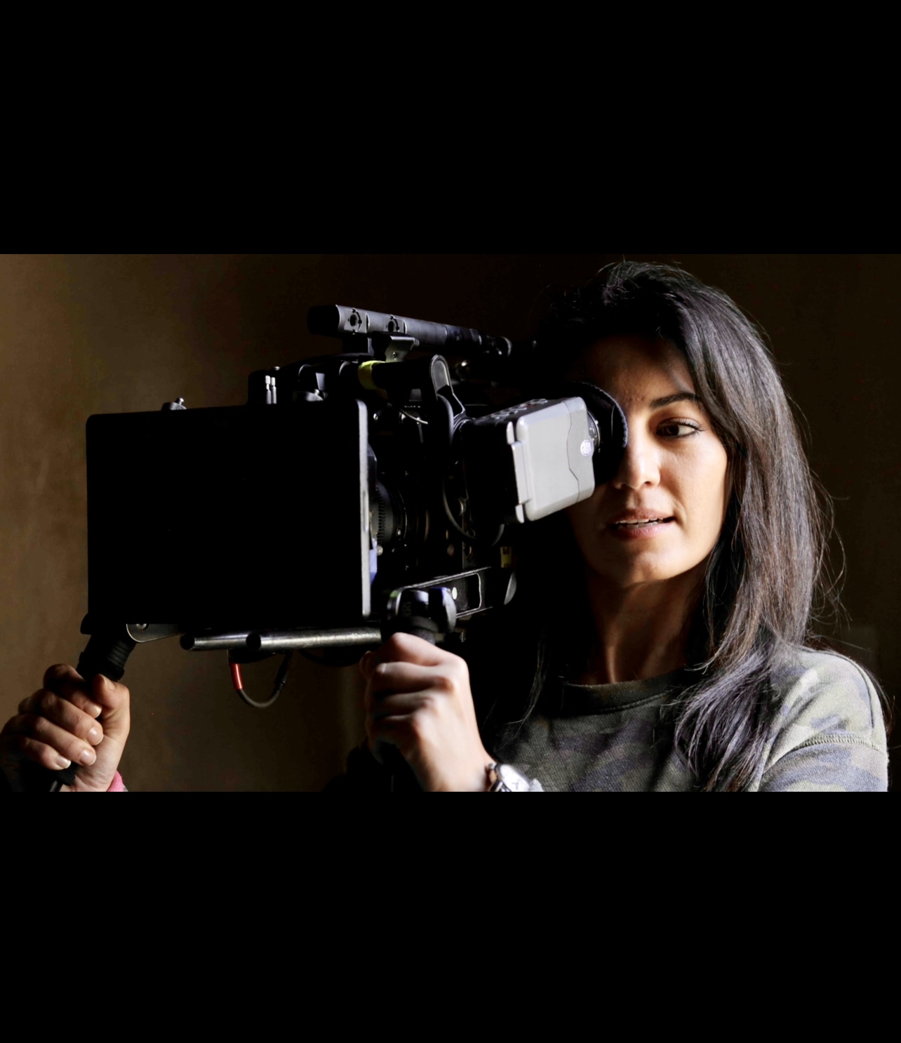 Le cinéma intimiste de Maryam Touzani capture une femme tenant une caméra sur un fond sombre.