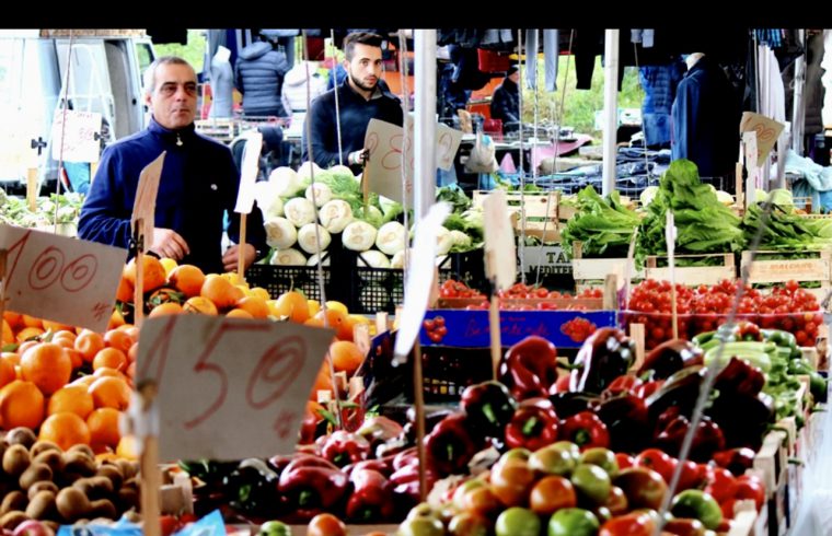 Un homme se tient dans un marché animé rempli de fruits et de légumes pendant la semaine de la cuisine italienne.
