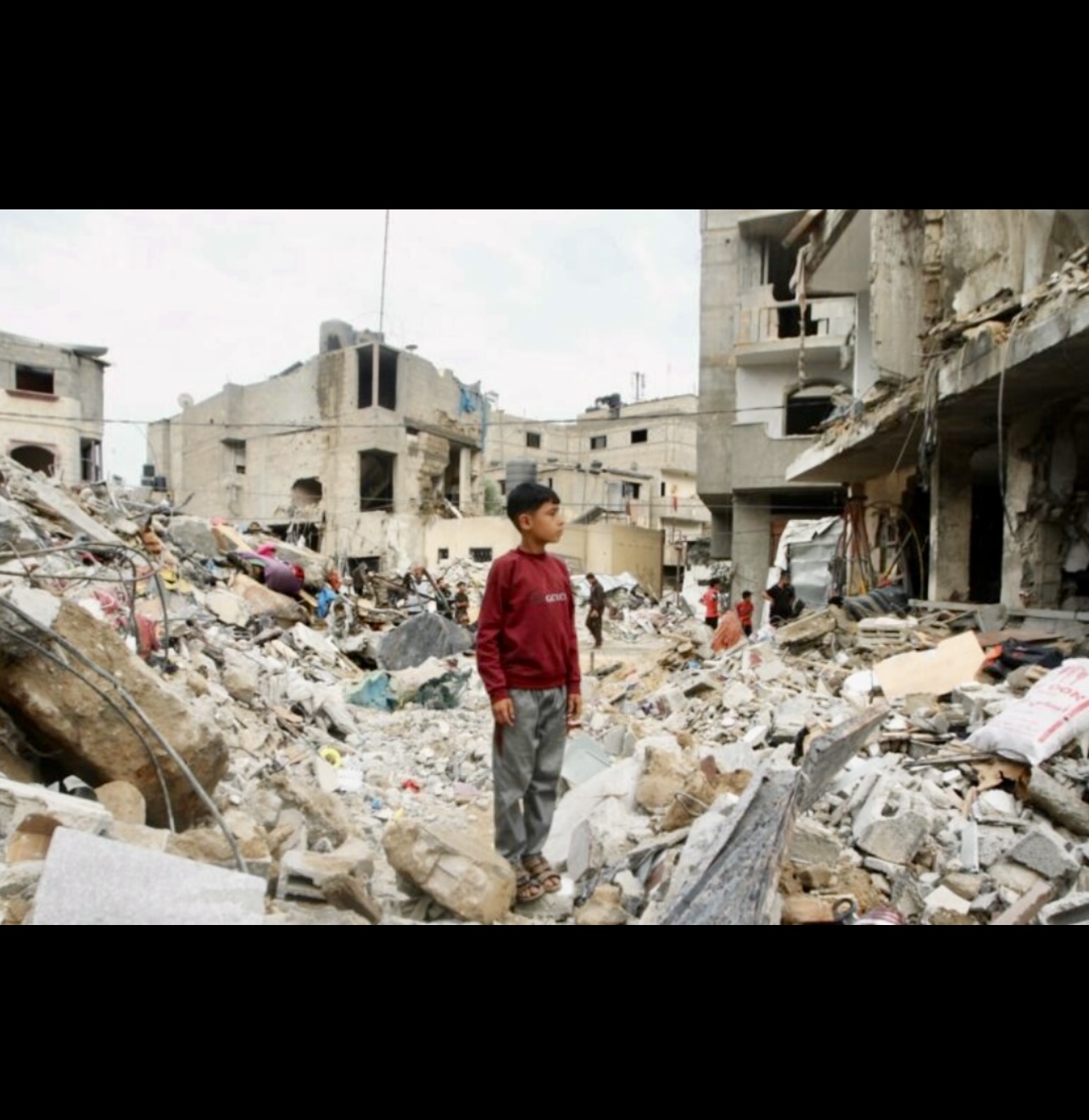 Un garçon palestinien se tient debout dans les décombres d’un bâtiment détruit.