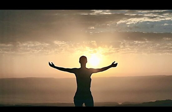 La silhouette d’une personne debout au sommet d’une colline, les bras tendus, évoquant un sentiment de spiritualité.