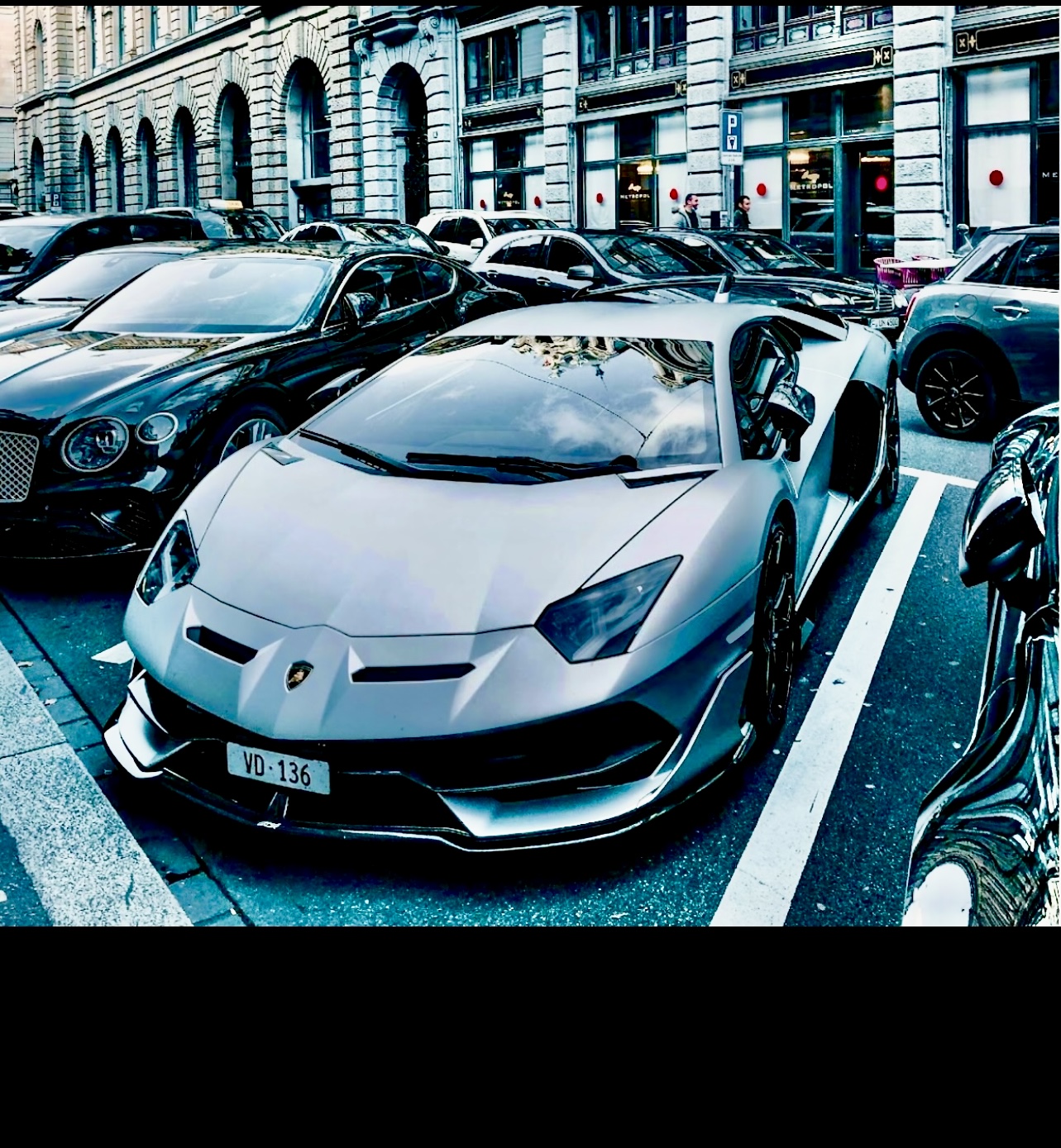 Deux voitures de luxe, une Lamborghini et une Bentley, sont stationnées dans un parking.